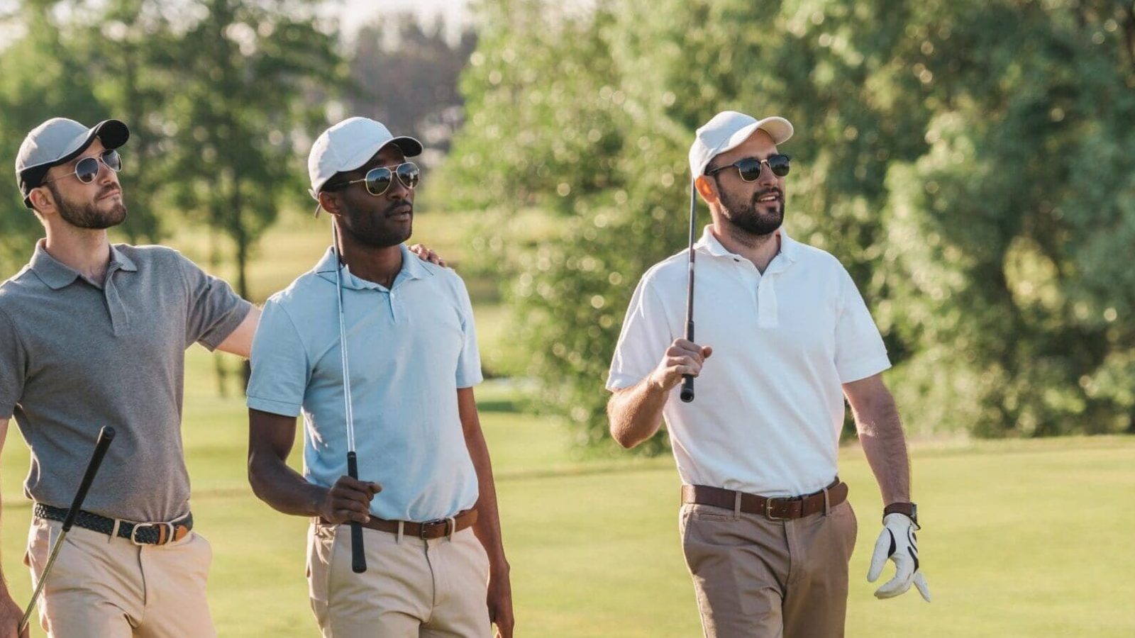 Golfers walking on sunny course with clubs.