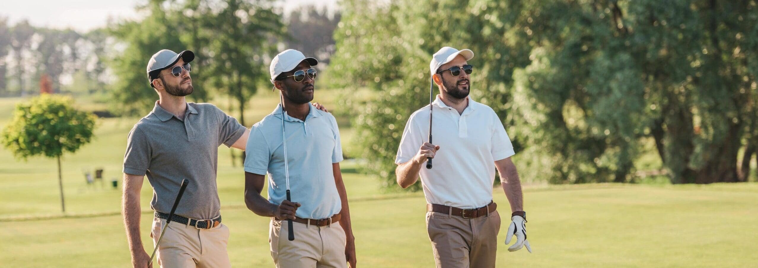 Golfers walking on sunny course with clubs.